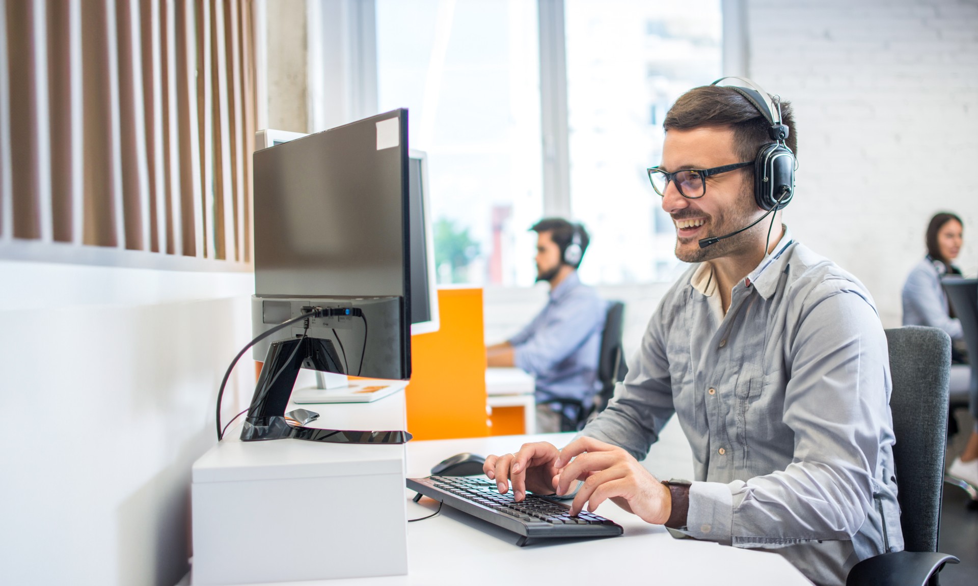 Friendly service agent using computer and talking to customer in call centre.